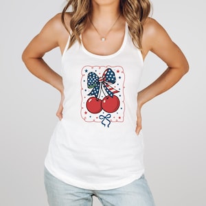Könnte beinhalten: Weißes Tanktop mit einem patriotischen Kirschdesign. Die Grafik zeigt zwei rote Kirschen, eine Schleife mit Sternen- und Streifenmuster und einen rot-weiß-blauen Rand mit Sternen.