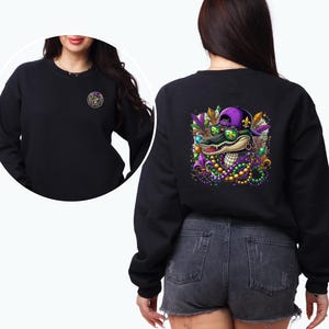 May include: Black sweatshirt with a colorful graphic of an alligator wearing sunglasses and a purple hat with beads and fleur-de-lis. The alligator is surrounded by green, purple, and gold beads.