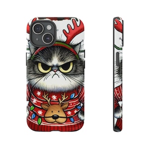 May include: A phone case with a cartoon illustration of a grumpy cat wearing a red and white Christmas sweater with a reindeer design. The cat has black and white fur and a red nose.