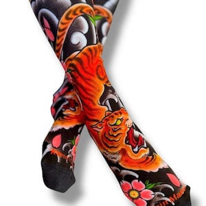 May include: A pair of black socks with a colorful Japanese-style tiger design. The socks feature a tiger with orange and black stripes, pink cherry blossoms, and blue and white clouds. The socks are made of a soft, comfortable material and are perfect for adding a touch of style to any outfit.