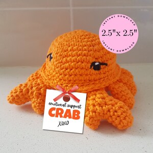 May include: Orange crocheted crab with black eyes and a white tag that says "emotional support crab xoxo". The tag is tied with a red ribbon. The crab is 2.5 inches by 2.5 inches.