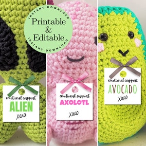 May include: Three crocheted plushies, each with a different design and color. The plushies are green, pink, and green. Each plush has a tag attached to it with the text "emotional support" and the name of the plush. The green plush is an alien, the pink plush is an axolotl, and the green plush is an avocado.
