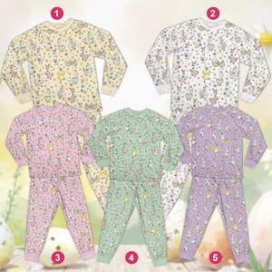 May include: Five sets of children's pajamas in various pastel colors. Each set includes a long-sleeved top and matching pants, all patterned with Easter-themed illustrations of bunnies and geese. The colors include pale yellow, white, pink, mint green, and lavender.