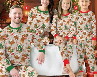 May include: Matching family Christmas pajamas featuring a gingerbread man and tree pattern on a beige background. The pajamas have green and red trim. The family is sitting in front of a Christmas tree and fireplace.