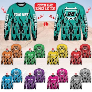 Puede incluir: Camisetas de manga larga en varios colores, con un diseño de llamas y espacio para texto y números personalizados. Las camisetas tienen cuello redondo y son adecuadas para deportes o uso casual. El texto "YOUR TEXT" es visible en las mangas.