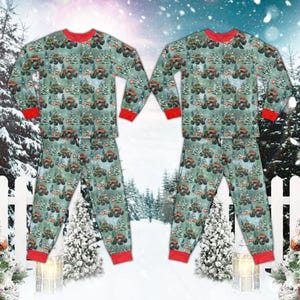 May include: Matching pajama set featuring a green and white pattern of monster trucks and Christmas trees. The long-sleeved top and pants have red trim at the cuffs and neckline. The pajamas are displayed against a snowy winter scene.