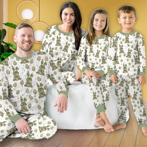 May include: A family of four wearing matching white pajamas with a green and brown Easter bunny and egg pattern. The pajamas have long sleeves and pants.