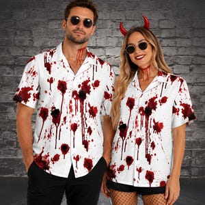 May include: Two white short-sleeved button-down shirts featuring a red blood splatter pattern and dark circular bullet hole graphics. The shirts have a classic collar, a front button closure, and a lightweight fabric construction with a print.
