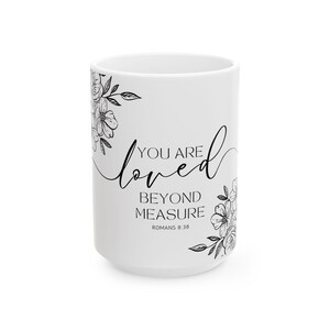 K&ouml;nnte beinhalten: Wei&szlig;e Keramiktasse mit schwarzem Blumendesign und dem Text "You are loved beyond measure Romans 8:38"