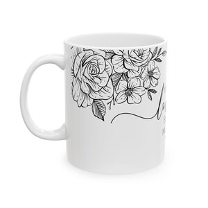 K&ouml;nnte beinhalten: Wei&szlig;e Keramiktasse mit schwarzem Blumendesign und dem Text "Let your light shine" an der Seite.