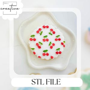 Puede incluir: Una galleta redonda y blanca glaseada, decorada con cerezas rojas y hojas verdes. La galleta está sobre un plato blanco en forma de estrella. El texto "STL FILE" está en la parte inferior de la imagen.