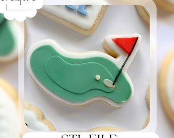 Puede incluir: Una galleta con temática de golf decorada con glaseado verde para parecerse a un green de golf, una bandera roja y un borde blanco. La galleta tiene el texto "STL FILE" en la parte inferior. La galleta está rodeada de otras galletas.