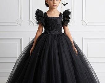May include: A black floor-length dress with a square neckline, ruffled tulle sleeves, and a full skirt. The bodice features black floral lace appliqués. A decorative headpiece includes orange pumpkin accents, black bat cutouts, and hanging chains.