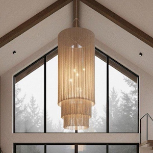 May include: A contemporary living room with a high, vaulted ceiling and large windows overlooking a misty forest. The room features a neutral colour scheme, a fireplace, a large sofa, and a decorative chandelier. The space is designed with a minimalist aesthetic.