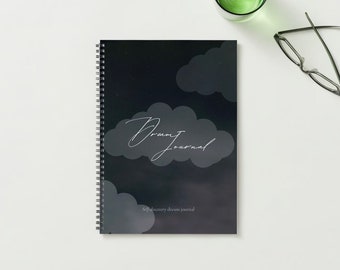 May include: A black spiral bound journal with a dark blue starry sky background and white clouds. The text "Dream Journal" is written in white cursive script on a cloud. The text "Self-discovery dream journal" is written in white at the bottom of the journal.