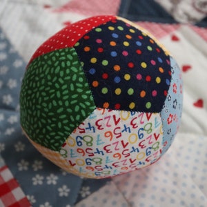 May include: A multi-colored fabric ball with a patchwork design. The ball is made of different fabrics with various patterns, including polka dots, numbers, and small green shapes.