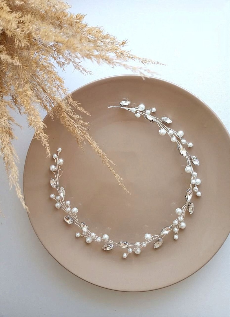 May include: A silver and pearl hair vine with a delicate design. The vine is made of silver wire with small pearl beads and clear rhinestones. It is a beautiful and elegant hair accessory for a wedding or special occasion.