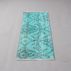 May include: A rectangular runner rug featuring a vibrant turquoise background with a dark charcoal gray floral and vine pattern. The rug has a distressed, weathered texture throughout and is finished with short white fringe on both ends.