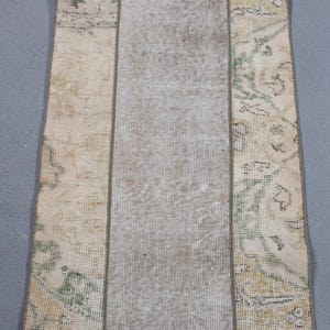 May include: Rectangular rug with a central light gray panel flanked by panels with faded floral patterns in green, yellow, and brown. The rug has a distressed, vintage appearance, suggesting it is handmade.