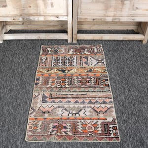 Könnte beinhalten: Ein rechteckiger Teppich mit einem Patchwork-Design aus horizontalen Bändern mit komplexen geometrischen Mustern in gedeckten Orange-, Braun-, Grau- und Cremetönen. Der Teppich weist eine abgenutzte Textur mit verschiedenen Motiven wie Rauten, Zickzacklinien und blumenartigen Formen auf seiner gesamten Oberfläche auf.