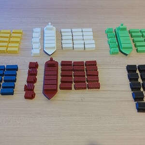 May include: A set of colourful cargo containers and ships for a board game. The containers are in various colours, including yellow, green, blue, red, white and black. The ships are white, yellow and red.
