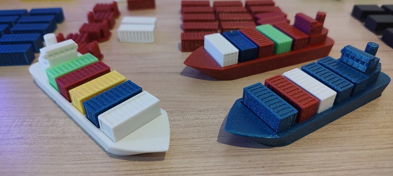May include: A set of three toy cargo ships with colourful containers. The ships are made of white, red and blue plastic. The containers are arranged in rows on the ships' decks. The ships are sitting on a wooden surface.