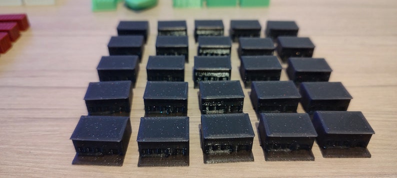 May include: A set of 24 black plastic miniature buildings, arranged in a grid pattern. The buildings are all the same size and shape, with a flat roof and a simple rectangular design.