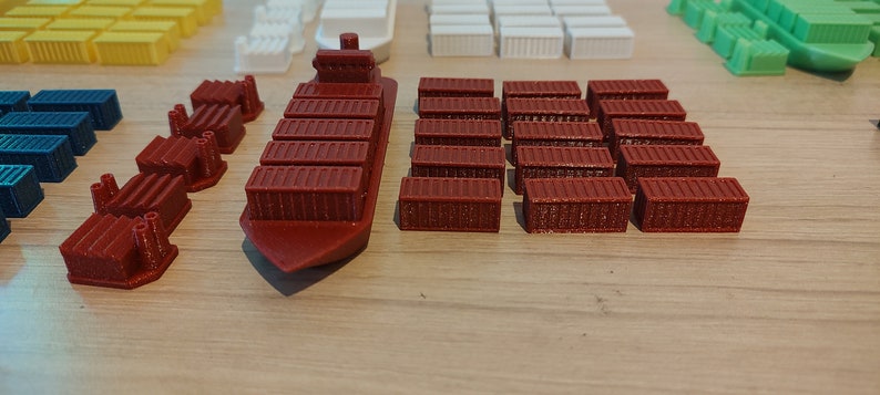 May include: A red cargo ship with a row of containers on deck, along with a collection of red, blue, white, and yellow containers.