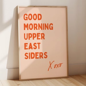 Könnte beinhalten: Ein gerahmter Kunstdruck mit den Worten "GOOD MORNING UPPER EAST SIDERS" in orangefarbenen Buchstaben auf einem pfirsichfarbenen Hintergrund. Der Druck enthält das handgeschriebene Wort "Xoxo" in Orange. Der Rahmen ist hellbraun.