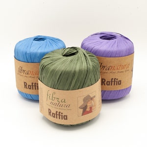 Può includere: Tre rocchetti di filo di rafia blu, verde e viola. I rocchetti sono etichettati con "fibra natura" e "Raffia".