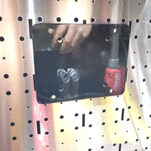 Peut inclure: Un support métallique noir monté sur une surface métallique perforée. Un outil rouge et gris est fixé au support. La surface métallique présente de nombreux petits trous et fentes rectangulaires.