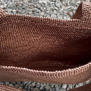 May include: A brown crocheted tote bag with a rectangular shape and two handles. The bag is made of a textured, woven material. The interior of the bag is visible, showing the open space for storage.