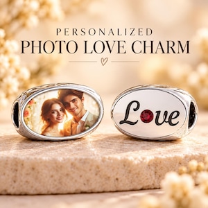 May include: Two oval silver charms. One charm features a colour photograph of a couple. The other charm has the word Love in black script with a small red crystal replacing the letter o. The text Personalized Photo Love Charm is above them.