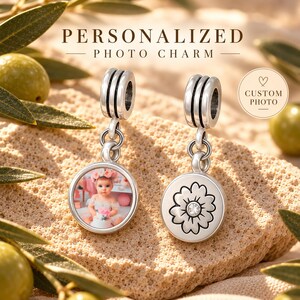 May include: Two silver-toned metal charms with a cylindrical bail. One charm features a circular inset with a photograph of a child wearing a floral crown. The other charm displays an engraved flower design with a small clear stone in the centre.