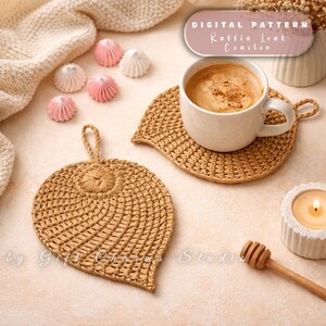 Puede incluir: Dos posavasos de rafia con forma de hoja, uno con una taza de café blanca. Los posavasos son de color marrón claro. La imagen también incluye una vela, merengues y el texto "DIGITAL PATTERN Raffia Leaf Coaster."