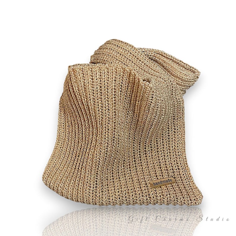 May include: A gold-colored, handmade knitted hat with a wide brim. The hat is made of a textured yarn and features a small, rectangular tag that reads "handmade". The hat is displayed on a white background with a slight reflection.
