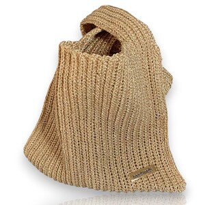 May include: A gold-colored, knitted tote bag with a handle. The bag has a rectangular shape with a wide opening and a small, rectangular tag that reads "handmade". The bag is made of a shiny, textured material.