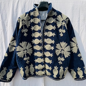 Pode incluir: Casaco azul marinho com intrincados bordados florais dourados. O casaco apresenta uma gola alta e um forro listrado. O bordado detalhado cobre a frente e as mangas, criando um visual texturizado e decorativo.