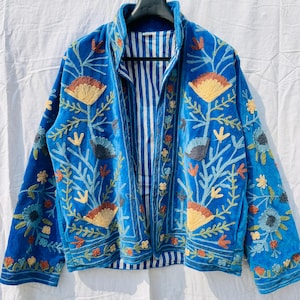 May include: A vibrant blue jacket with intricate floral embroidery in shades of yellow, orange, and green. The jacket features a striped lining and a high collar. The embroidery creates a textured, artistic design.