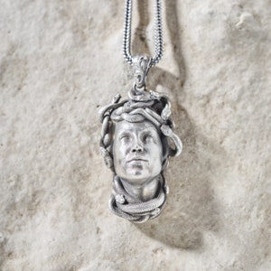 Könnte beinhalten: Eine silberne Halskette mit einem Anhänger, der eine detaillierte Skulptur eines Frauenkopfes mit Schlangen um den Kopf zeigt.