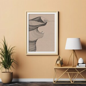 May include: A framed black and white line drawing of a surfer riding a wave. The drawing is on a beige background and is framed in a light wood frame. The frame is hanging on a light orange wall.