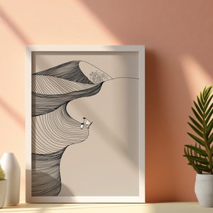 May include: A white framed print with a black and white line drawing of a desert landscape with two figures sitting on a dune. The background is a light beige color.