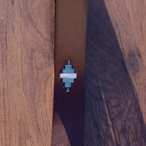 Könnte beinhalten: Ein brauner Ledergürtel mit einer silbernen Schnalle und zwei weißen und blauen geometrischen Mustern.