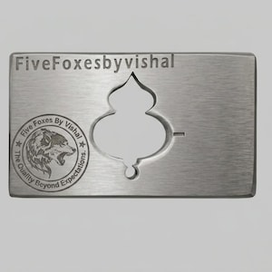 Może przedstawiać: Srebrzysty metalowy stempel i pasująca prostokątna metalowa płytka z wycięciem. Płytka zawiera napis FiveFoxesbyvishal oraz okrągłe logo z głową lisa i napisem Five Foxes By Vishal The Quality Beyond Expectations.