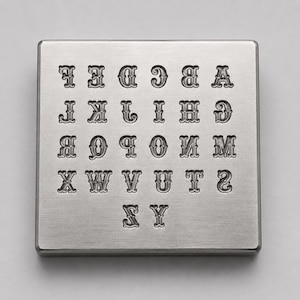 Könnte beinhalten: Eine quadratische, silberfarbene Metallplatte mit einem eingeprägten Alphabet von A bis Z. Die Buchstaben sind in fünf Reihen angeordnet, wobei jedes Zeichen einen dekorativen Serifenschriftstil aufweist. Die Oberfläche der Metallplatte ist gebürstet.
