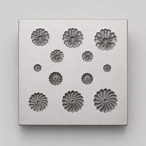 May include: A square silver-toned metal mould featuring twelve recessed floral patterns of varying sizes. The design includes three rows of circular flower impressions with radiating petals, arranged in a symmetrical grid on the flat surface.