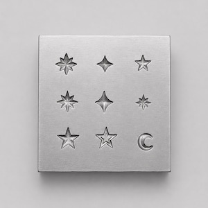 Peut inclure: Un bloc de marquage carré en métal argenté présentant une grille de neuf symboles célestes gravés. Le motif comprend diverses formes d'étoiles, notamment des étoiles à huit, quatre et cinq branches, ainsi qu'un symbole de croissant de lune.