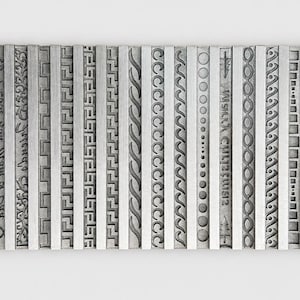 Peut inclure: Une plaque rectangulaire en métal argenté présentant une série de colonnes verticales, chacune gaufrée avec des motifs répétitifs distincts incluant des cœurs, des formes géométriques, des grecques, des tresses, des cercles et le texte Merry Christmas.