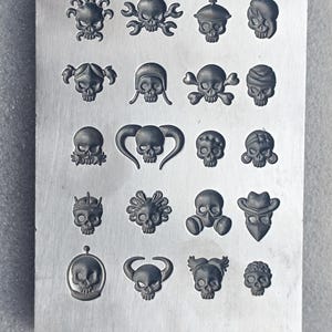 May include: A metal plate with a series of embossed skull designs. The skulls vary in style, some with accessories like hats, pigtails, and gas masks. The plate is a light gray color.