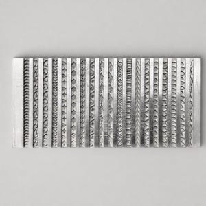 Op de afbeelding: Een rechthoekige, zilverkleurige metalen plaat met twintig verticale kolommen van verschillende reliëfpatronen. Elke kolom toont een uniek herhalend ontwerp, waaronder geometrische vormen, florale motieven, golven en lineaire texturen.